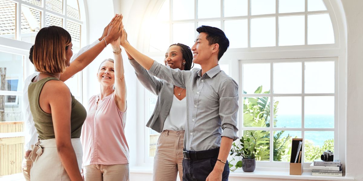 Real estate franchise team members celebrating with a high five in a bright office.