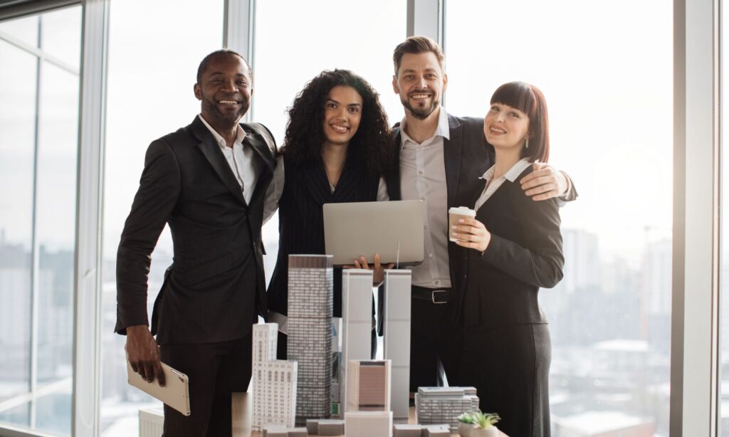 Real estate franchise team in formal attire, standing together in an office overlooking a city.