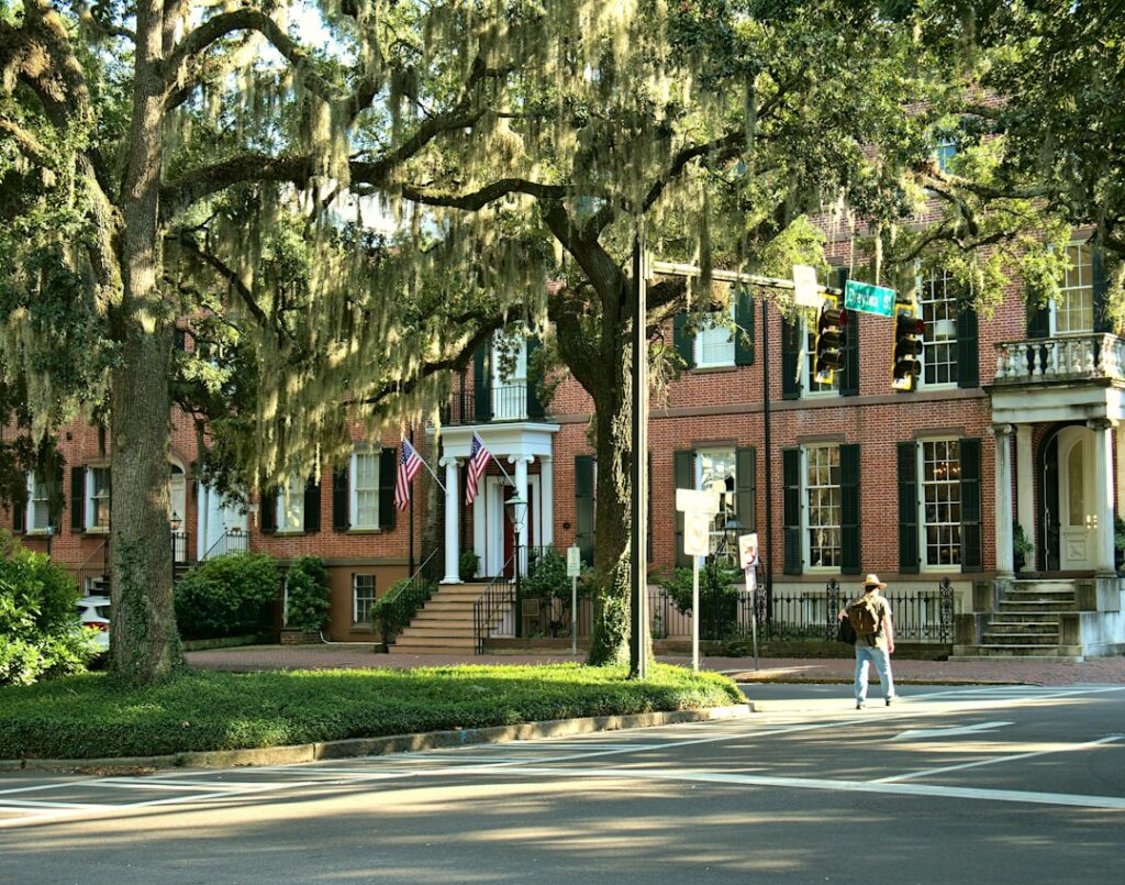 Classic historic home in Savannah, Georgia, framed by live oak trees with Spanish moss on a bright, sunny day, evoking a s...