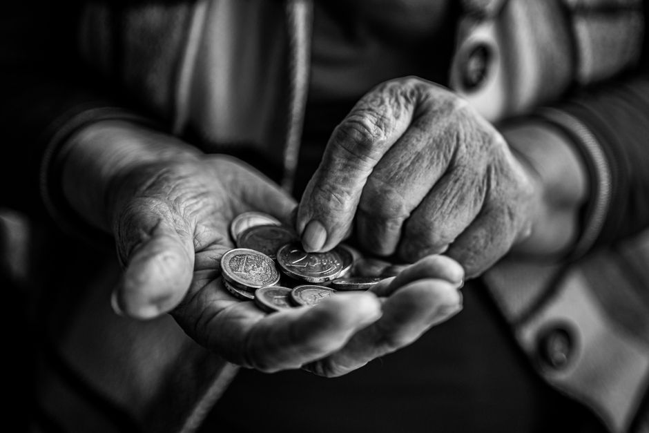 A minimalist photo of hands balancing a small house model against a stack of coins, illustrating the financial choice between a flat-fee and traditional commission.