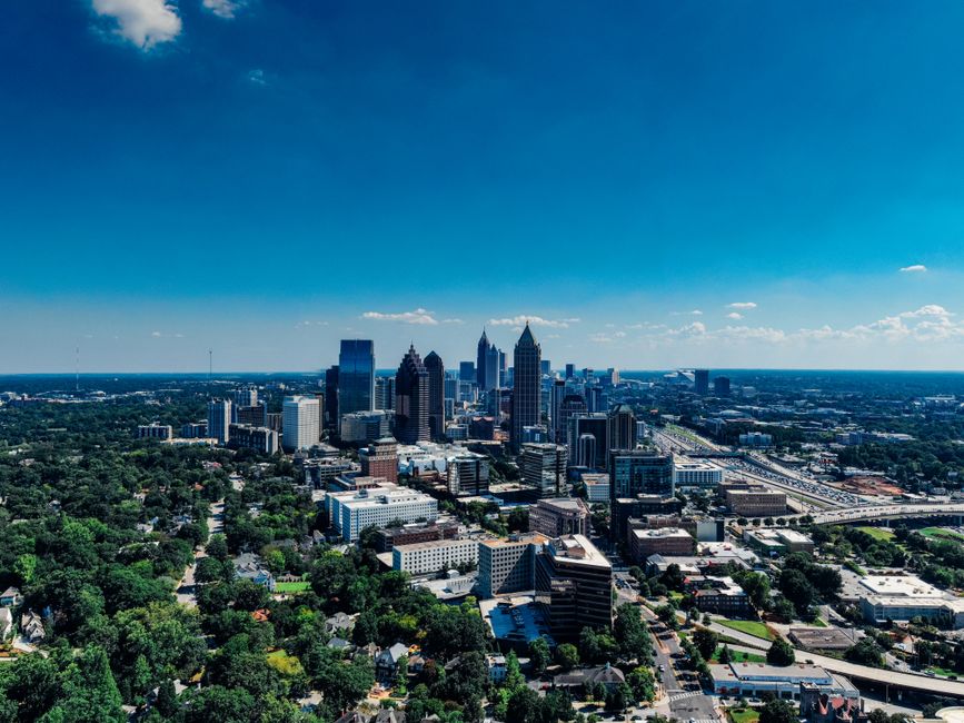 A sunlit street in a modern Atlanta neighborhood, with sleek corporate buildings and contemporary residential architecture side-by-side, illustrating the convenience of a short commute.